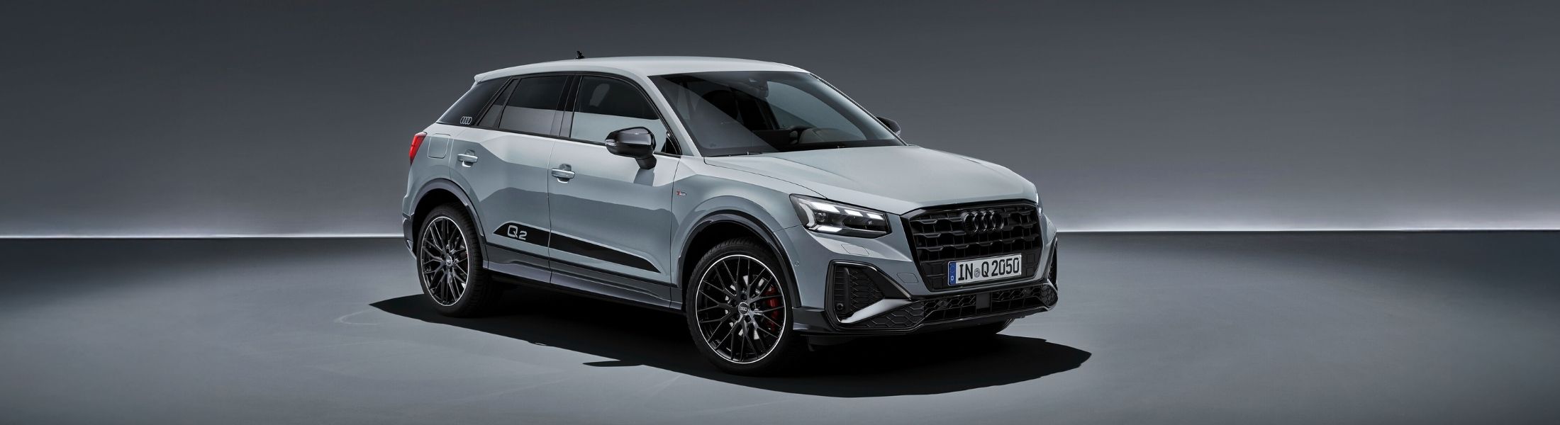 grauer Audi Q2 von schräg vorne auf grauem Hinterg