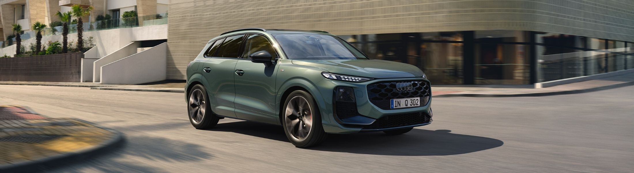 Grüner Audi Q3 von schräg vorne fährt in einer Sta