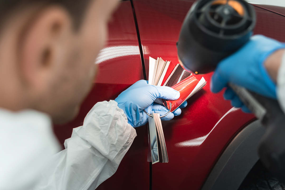 Lackierer vergleicht Farbkarte mit Autolack